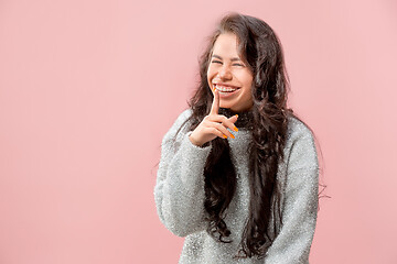 Image showing The young woman whispering a secret behind her hand pink background