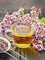 Image showing Tea of oregano in cup with strainer on dark wooden board