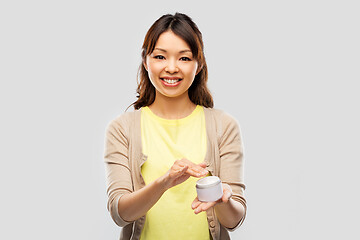 Image showing happy young asian woman holding jar of moisturizer