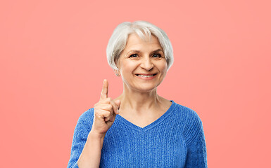 Image showing smiling senior woman pointing finger up over pink