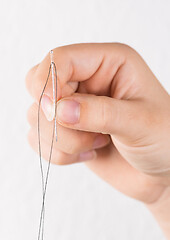 Image showing Detail of hand holding needle with thread on white background