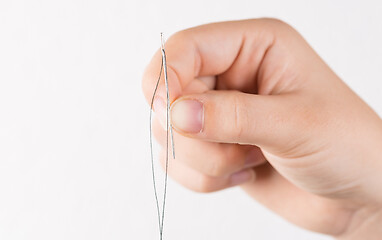 Image showing Detail of hand holding needle with thread on white background