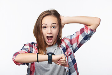 Image showing Shocked teenage girl holding hand with wrist watch and looking at camera shouting