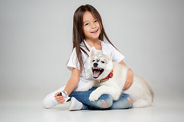 Image showing Portrait of a joyful little girl having fun with siberian husky puppy on the floor at studio