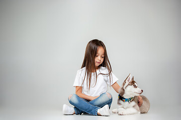 Image showing Portrait of a joyful little girl having fun with siberian husky puppy on the floor at studio