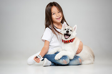 Image showing Portrait of a joyful little girl having fun with siberian husky puppy on the floor at studio