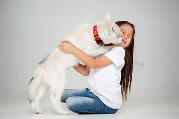 Image showing Portrait of a joyful little girl having fun with siberian husky puppy on the floor at studio