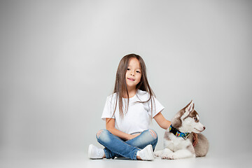 Image showing Portrait of a joyful little girl having fun with siberian husky puppy on the floor at studio