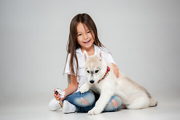 Image showing Portrait of a joyful little girl having fun with siberian husky puppy on the floor at studio