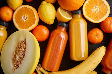 Image showing Mix of orange and yellow colored fruits and juices on black wooden background