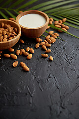 Image showing Amond seeds in wooden bowl, fresh natural milk placed on black stone background