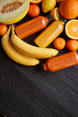 Image showing Yellow and orange fruits and botteled juices placed on black wooden background