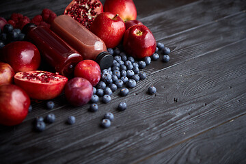 Image showing Various fresh red, purple black fruits. Mix of fruits and bottled juices on black