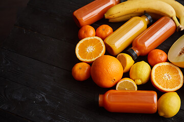 Image showing Yellow and orange fruits and botteled juices placed on black wooden background