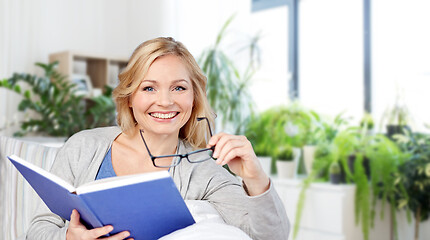 Image showing smiling woman reading book and sitting on couch