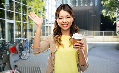 Image showing asian woman with coffee waving hand on city street