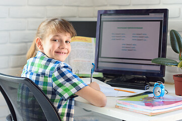 Image showing A satisfied child sits at a computer table and looks into the frame