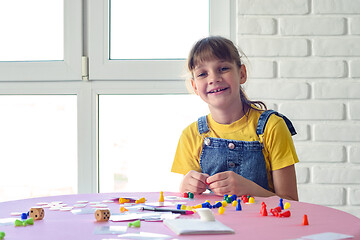 Image showing Cheerful girl plays board games at the table and looked into the frame