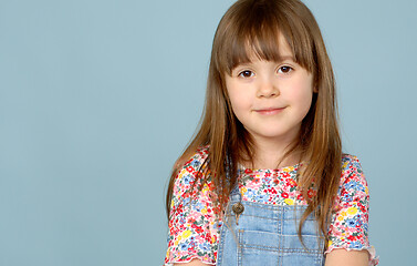 Image showing Sweet little girl 6-7 years old posing in dungarees jeans and flower pattern blouse on blue