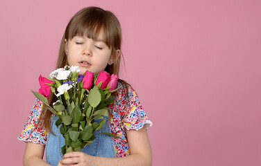 Image showing Cute smiling adorable child girl holding bouquet of spring flowers isolated on pink background