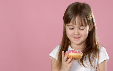 Image showing Studio portrait of a beautiful little girl holding a donut and smelling tasty flavour