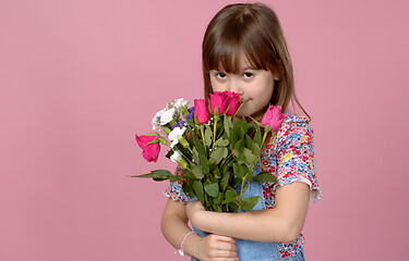 Image showing Sweet adorable young little girl holding bunch of fresh spring flowers. Wearing dungarees