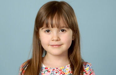 Image showing Potrait of nice smiling little girl with logng hair posing over blue background in studio