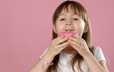 Image showing Cute young caucasian girl caught eating a sweet pink doughnut