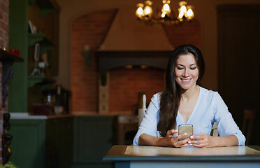 Image showing Smiling woman sitting and table and using smartphone