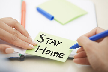 Image showing Hands of woman writing on adhesive note with Stay Home text