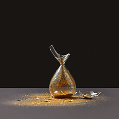 Image showing Brocken vintage sandglass with golden sand on a black duotone background.