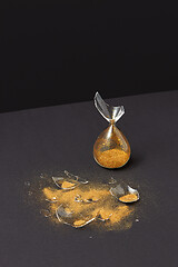Image showing Crashed outdated sandglass with golden sand on a black duotone background.