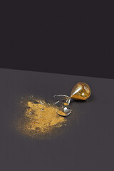 Image showing Crashed outdated hourglass with golden sand on a black duotone background.