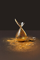 Image showing Cracked antique hourglass with golden sand on a black duotone background.