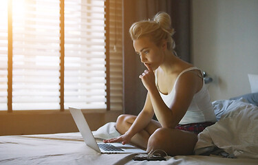 Image showing Beautiful young woman in pajamas sitting on bed with laptop