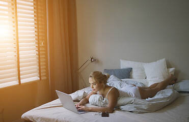 Image showing Sensual young woman in white tank top and panties lying on bed near laptop