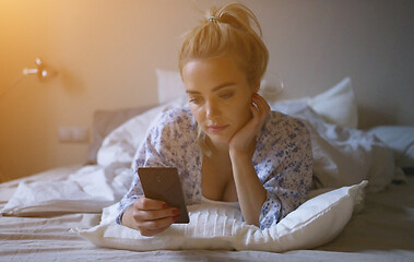 Image showing Lovely young woman with cute ponytail lying on comfortable bed and browsing smartphone