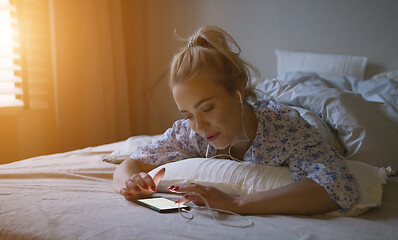 Image showing Charming young woman with ponytail listening to good music while lying on comfortable bed