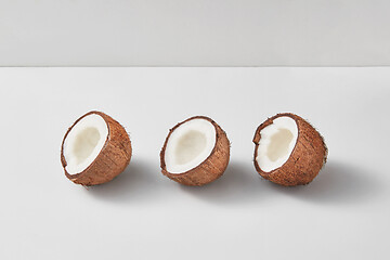 Image showing Three halves of fresh ripe organic coconut on a light grey background.