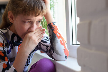Image showing Girl weeping bitterly at the window wipes her tears with her hand