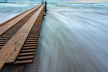 Image showing Wooden pier stretching into the distance, surf with blurry waves