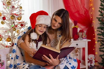Image showing Mom and daughter sit next to a Christmas tree and read a big boo