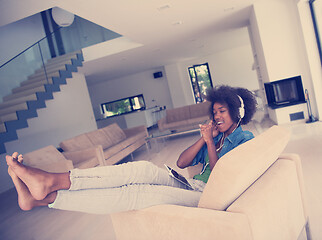 Image showing African american woman at home in chair with tablet and head pho