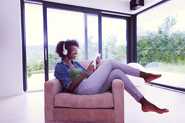 Image showing African american woman at home in chair with tablet and head pho