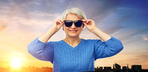 Image showing senior woman in sunglasses over sunset in city