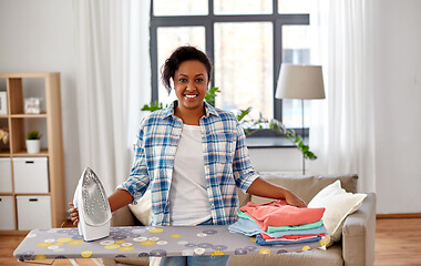 Image showing african american woman with ironed clothes at home