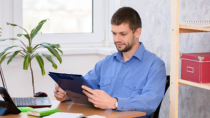 Image showing Office worker at the table reads documents in a folder