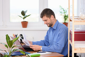 Image showing Successful young man reads documents while sitting at a table in the office