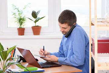 Image showing Businessman talking on the phone and taking notes in a notebook