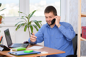 Image showing Office specialist talking on the phone and taking notes in a notebook